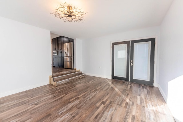 unfurnished living room with hardwood / wood-style floors, an inviting chandelier, and french doors