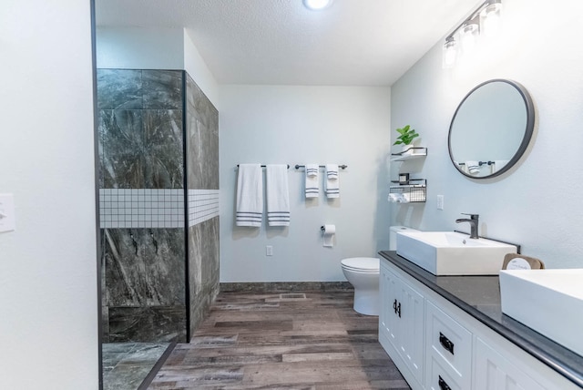 bathroom with vanity, toilet, a textured ceiling, tiled shower, and wood-type flooring