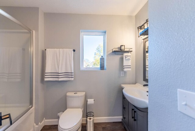 full bathroom with combined bath / shower with glass door, hardwood / wood-style floors, vanity, and toilet