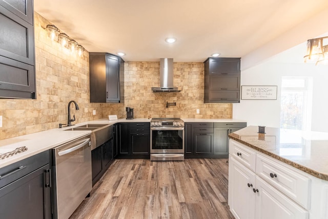 kitchen featuring stainless steel appliances, sink, wall chimney range hood, white cabinets, and light hardwood / wood-style floors