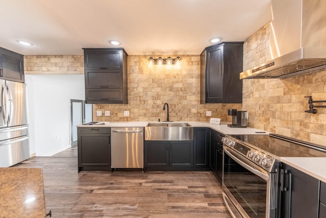 kitchen with dark wood-type flooring, wall chimney range hood, sink, decorative backsplash, and appliances with stainless steel finishes