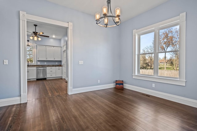 unfurnished dining area with ceiling fan with notable chandelier, a healthy amount of sunlight, and dark hardwood / wood-style floors