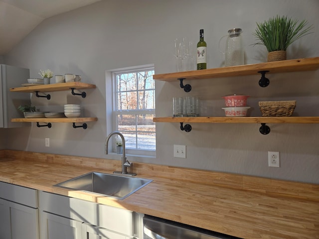 kitchen featuring lofted ceiling, sink, stainless steel dishwasher, butcher block countertops, and white cabinetry