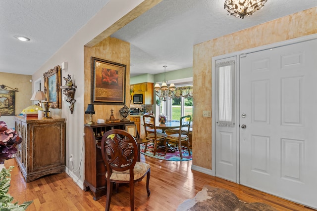 foyer entrance featuring light hardwood / wood-style flooring, a textured ceiling, and an inviting chandelier