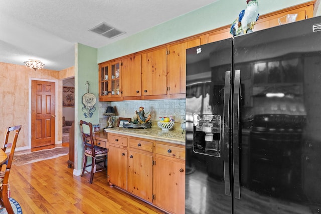 kitchen with backsplash, black fridge with ice dispenser, a textured ceiling, and light wood-type flooring