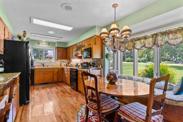 kitchen featuring black appliances, light hardwood / wood-style flooring, a textured ceiling, tasteful backsplash, and a notable chandelier