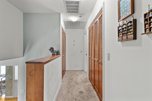 corridor with a textured ceiling and light carpet