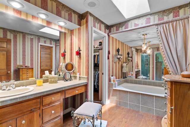 bathroom featuring a skylight, a relaxing tiled tub, a notable chandelier, vanity, and hardwood / wood-style flooring