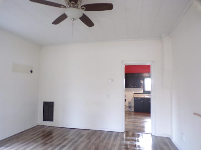 empty room featuring ceiling fan, crown molding, and dark wood-type flooring