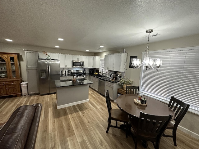 dining space with sink, light hardwood / wood-style floors, a textured ceiling, and an inviting chandelier