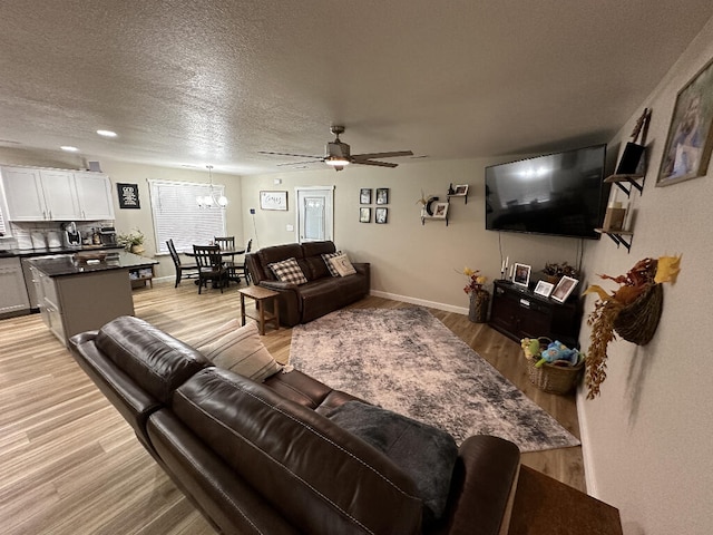 living room with a textured ceiling, light hardwood / wood-style flooring, and ceiling fan with notable chandelier