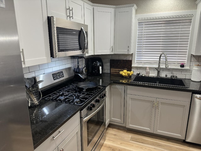 kitchen with sink, light hardwood / wood-style floors, dark stone counters, white cabinets, and appliances with stainless steel finishes