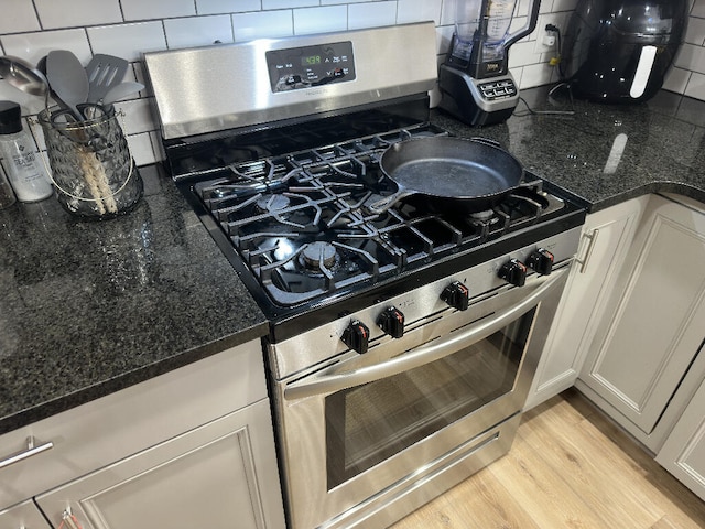 kitchen with backsplash, dark stone counters, light hardwood / wood-style flooring, white cabinets, and stainless steel range with gas stovetop