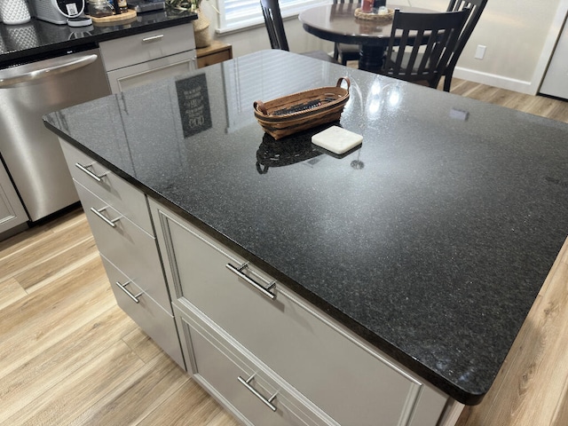 kitchen with dishwasher, light hardwood / wood-style floors, and dark stone countertops