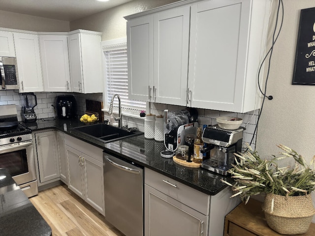 kitchen featuring appliances with stainless steel finishes, light wood-type flooring, backsplash, dark stone counters, and sink