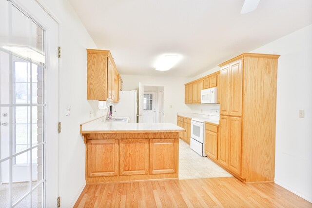 kitchen with kitchen peninsula, light brown cabinets, white appliances, and light hardwood / wood-style floors