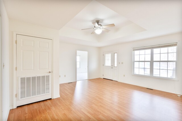 empty room featuring a raised ceiling, light hardwood / wood-style flooring, and ceiling fan