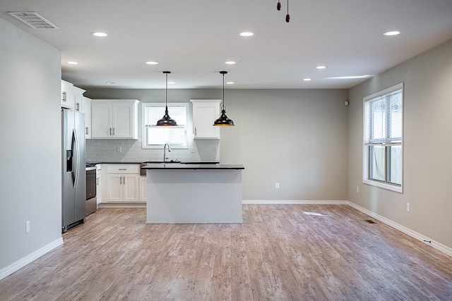 kitchen with light wood-type flooring, a healthy amount of sunlight, decorative light fixtures, and appliances with stainless steel finishes