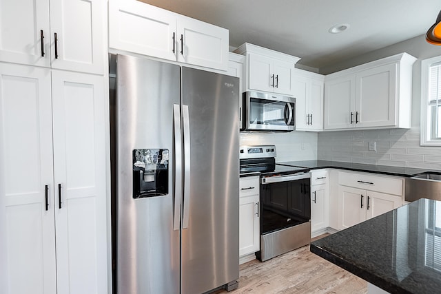 kitchen featuring white cabinets, light hardwood / wood-style flooring, dark stone countertops, appliances with stainless steel finishes, and tasteful backsplash