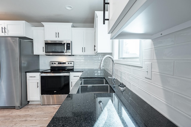 kitchen with dark stone counters, white cabinets, sink, appliances with stainless steel finishes, and light hardwood / wood-style floors