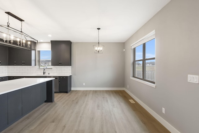 kitchen featuring decorative backsplash, light wood-type flooring, hanging light fixtures, and sink