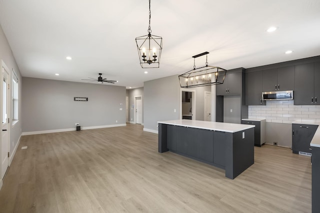 kitchen with pendant lighting, ceiling fan with notable chandelier, a center island, and light hardwood / wood-style floors