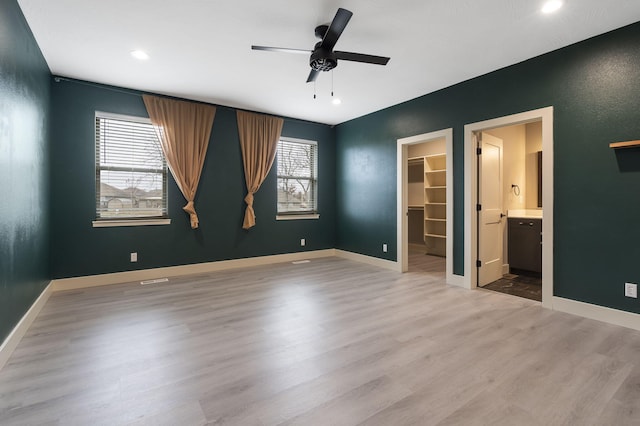 unfurnished bedroom featuring ceiling fan, light wood-type flooring, a spacious closet, and multiple windows