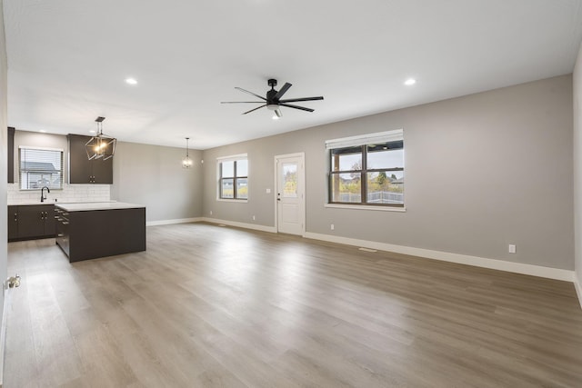 unfurnished living room with ceiling fan with notable chandelier, sink, and light hardwood / wood-style flooring