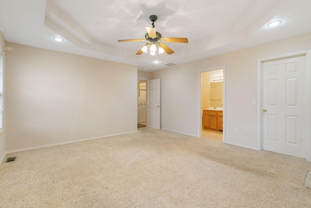 unfurnished bedroom with ensuite bathroom, ceiling fan, light colored carpet, and a tray ceiling