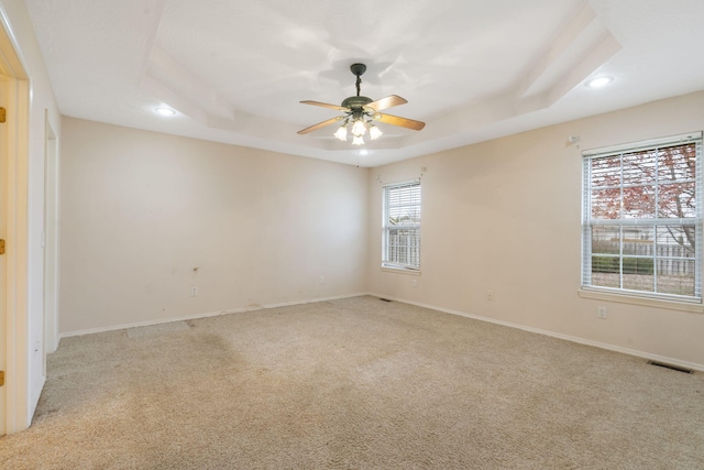 carpeted empty room with a tray ceiling, a wealth of natural light, and ceiling fan