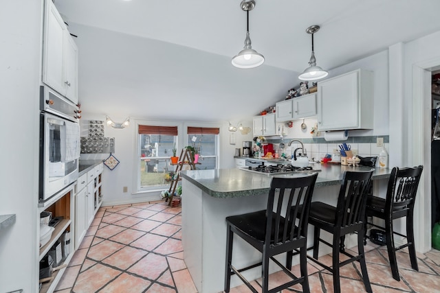 kitchen with a breakfast bar, white cabinets, oven, decorative backsplash, and kitchen peninsula