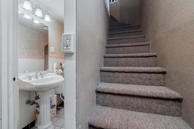 stairway featuring tile patterned floors, sink, and tile walls