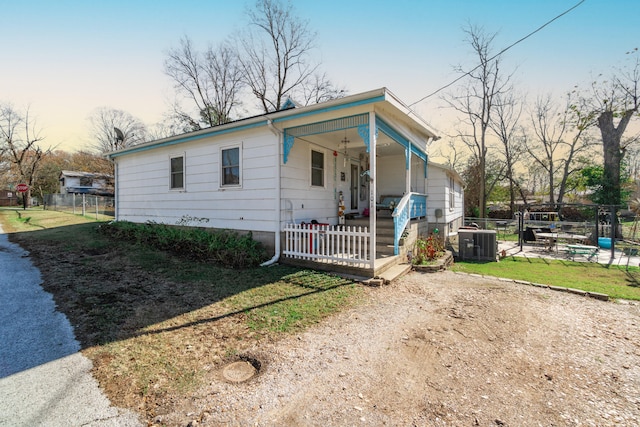 view of front facade featuring central AC unit, covered porch, and a yard