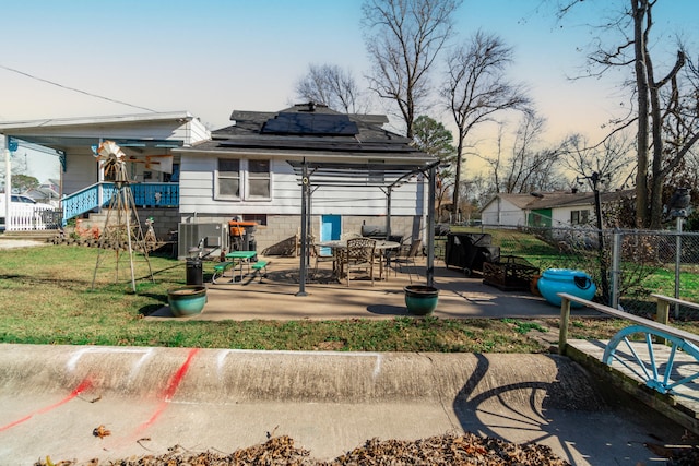 back house at dusk with a lawn, a patio, and solar panels