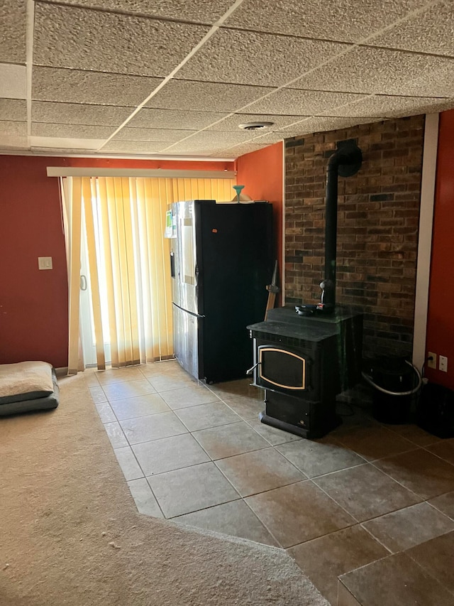 kitchen with a paneled ceiling, a wood stove, tile patterned floors, and stainless steel refrigerator