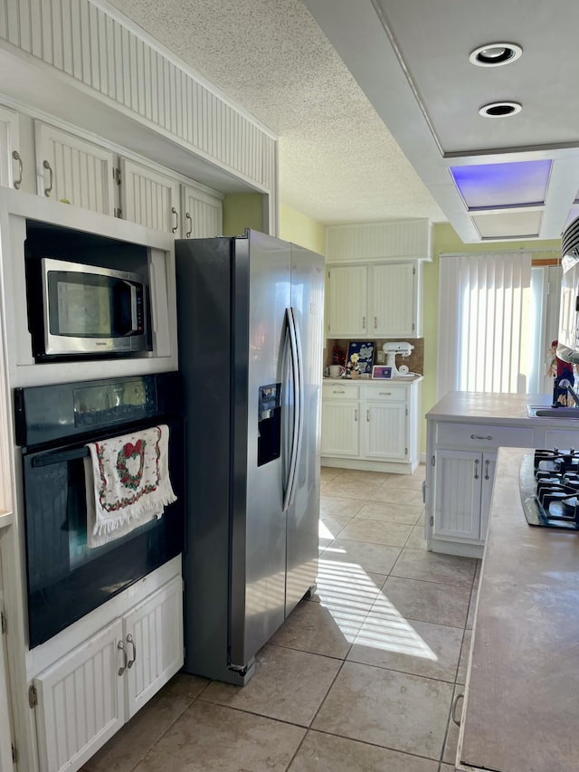 kitchen with light tile patterned floors, a textured ceiling, stainless steel appliances, and white cabinetry