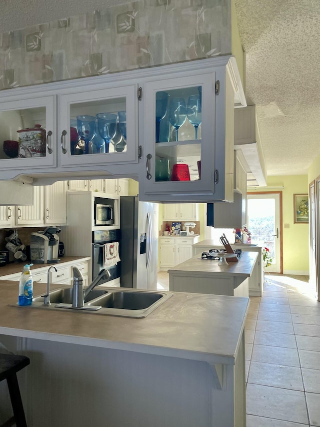 kitchen with kitchen peninsula, a textured ceiling, stainless steel appliances, sink, and white cabinetry