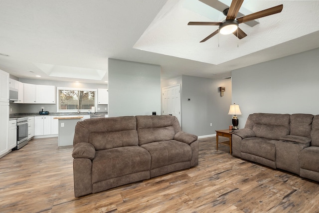 living room featuring a textured ceiling, light wood-type flooring, a raised ceiling, and ceiling fan