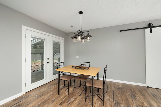 dining room featuring french doors, a barn door, a chandelier, a textured ceiling, and hardwood / wood-style flooring