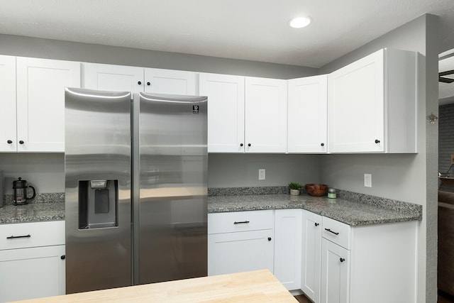 kitchen with dark stone countertops, white cabinetry, and stainless steel refrigerator with ice dispenser