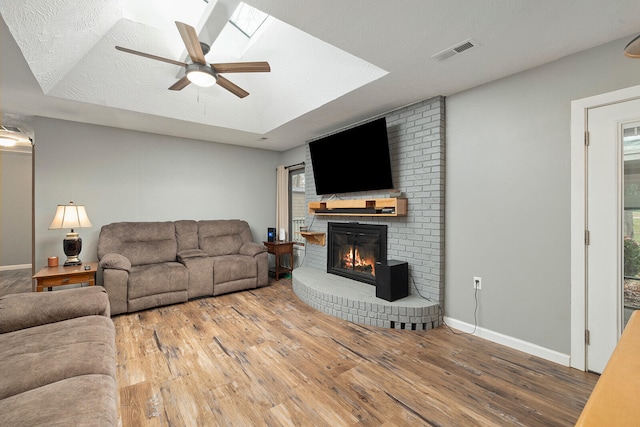 living room featuring ceiling fan, wood-type flooring, a textured ceiling, and a skylight