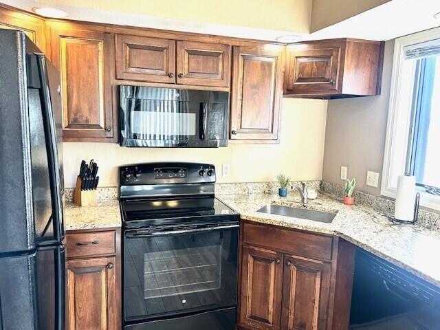 kitchen featuring sink, a wealth of natural light, light stone counters, and black appliances