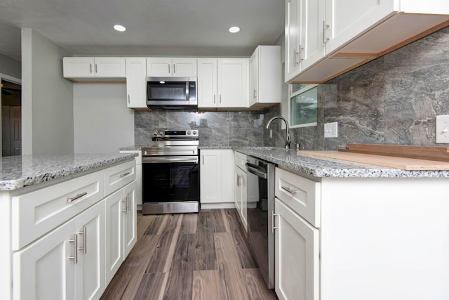 kitchen with appliances with stainless steel finishes, dark hardwood / wood-style flooring, tasteful backsplash, sink, and white cabinetry