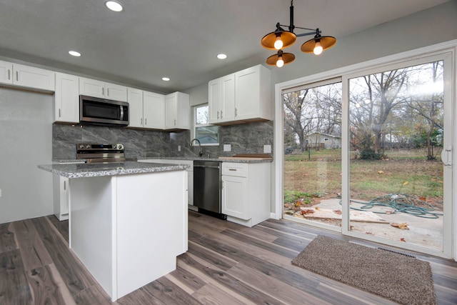 kitchen with white cabinets, dark hardwood / wood-style floors, appliances with stainless steel finishes, decorative light fixtures, and light stone counters