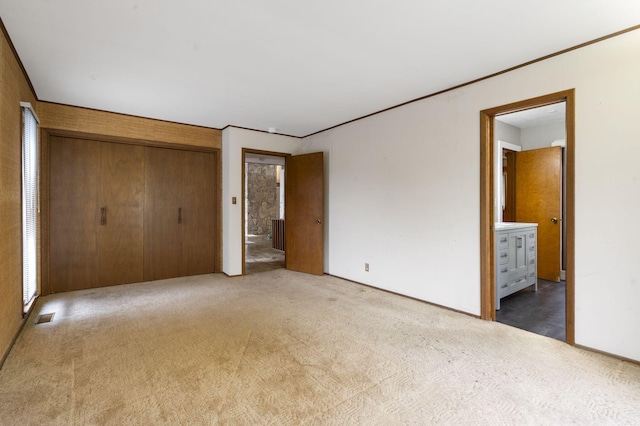 unfurnished bedroom with a closet, light carpet, and ensuite bath