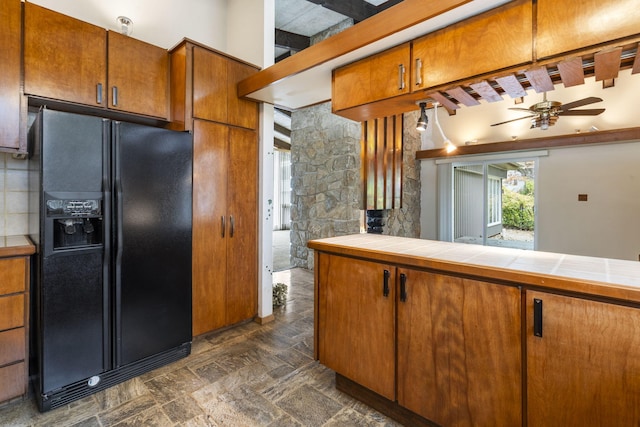 kitchen featuring tile countertops, black refrigerator with ice dispenser, beamed ceiling, and ceiling fan