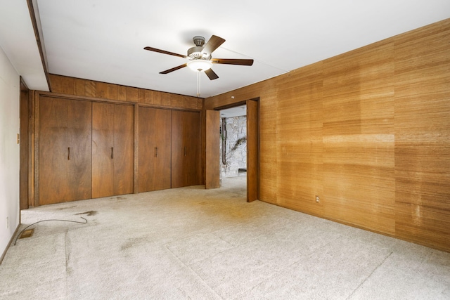 empty room featuring ceiling fan, wooden walls, and light colored carpet