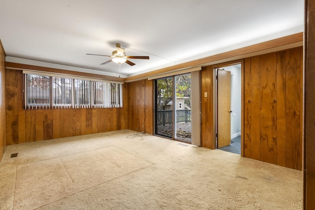 carpeted empty room featuring wood walls and ceiling fan