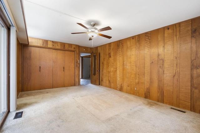 unfurnished bedroom featuring light carpet, a closet, ceiling fan, and wood walls