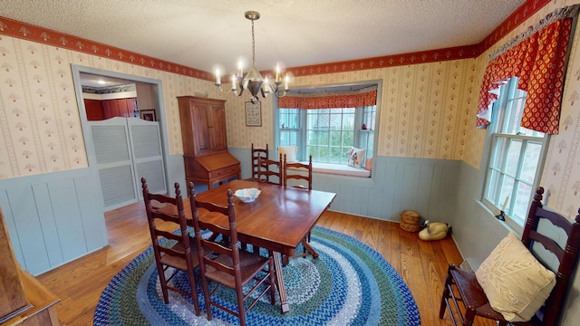 15047 E Peace Rd, Nevada, MO 64772 - dining room with light wood-style floors, a textured ceiling, a wainscoted wall, a chandelier, and wallpapered walls